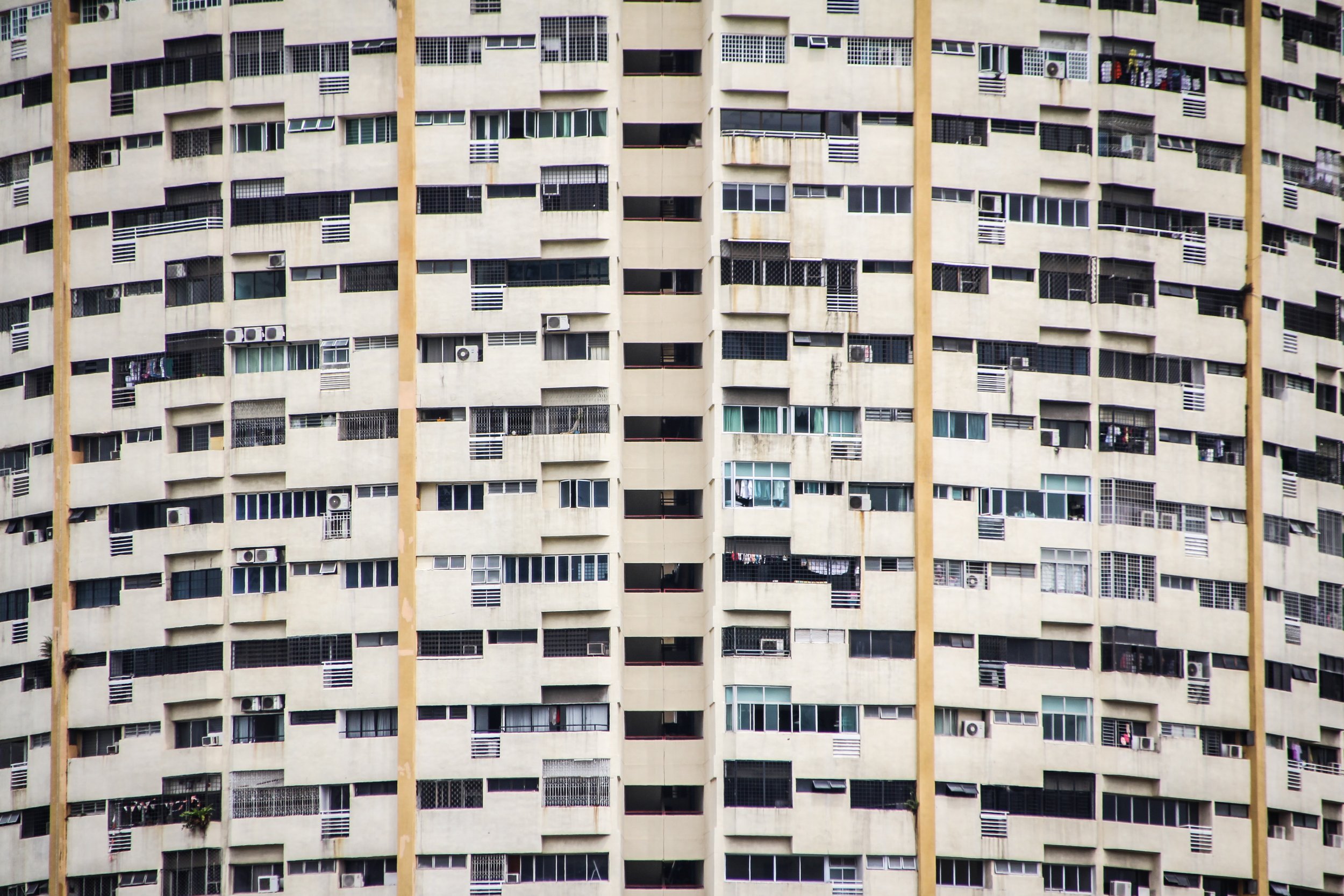 Facade of a large concrete apartment block filled with windows, balconies and air conditioning units