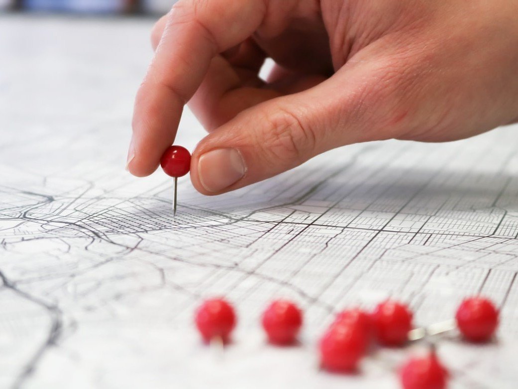 Hand placing a red pin into a printed street map