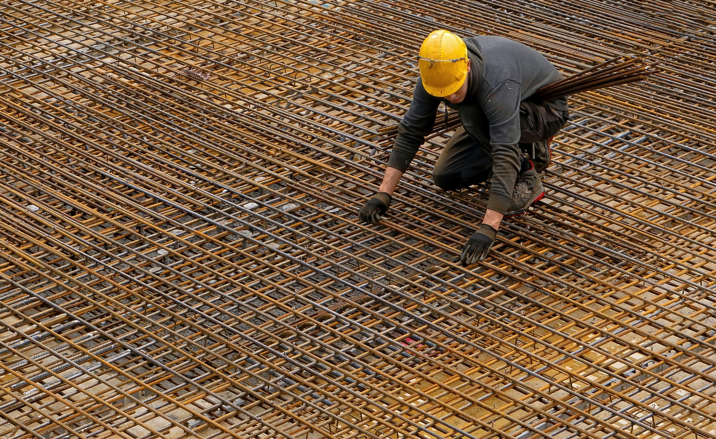 Construction worker in a hard hat tying reinforcing bar across a concrete deck